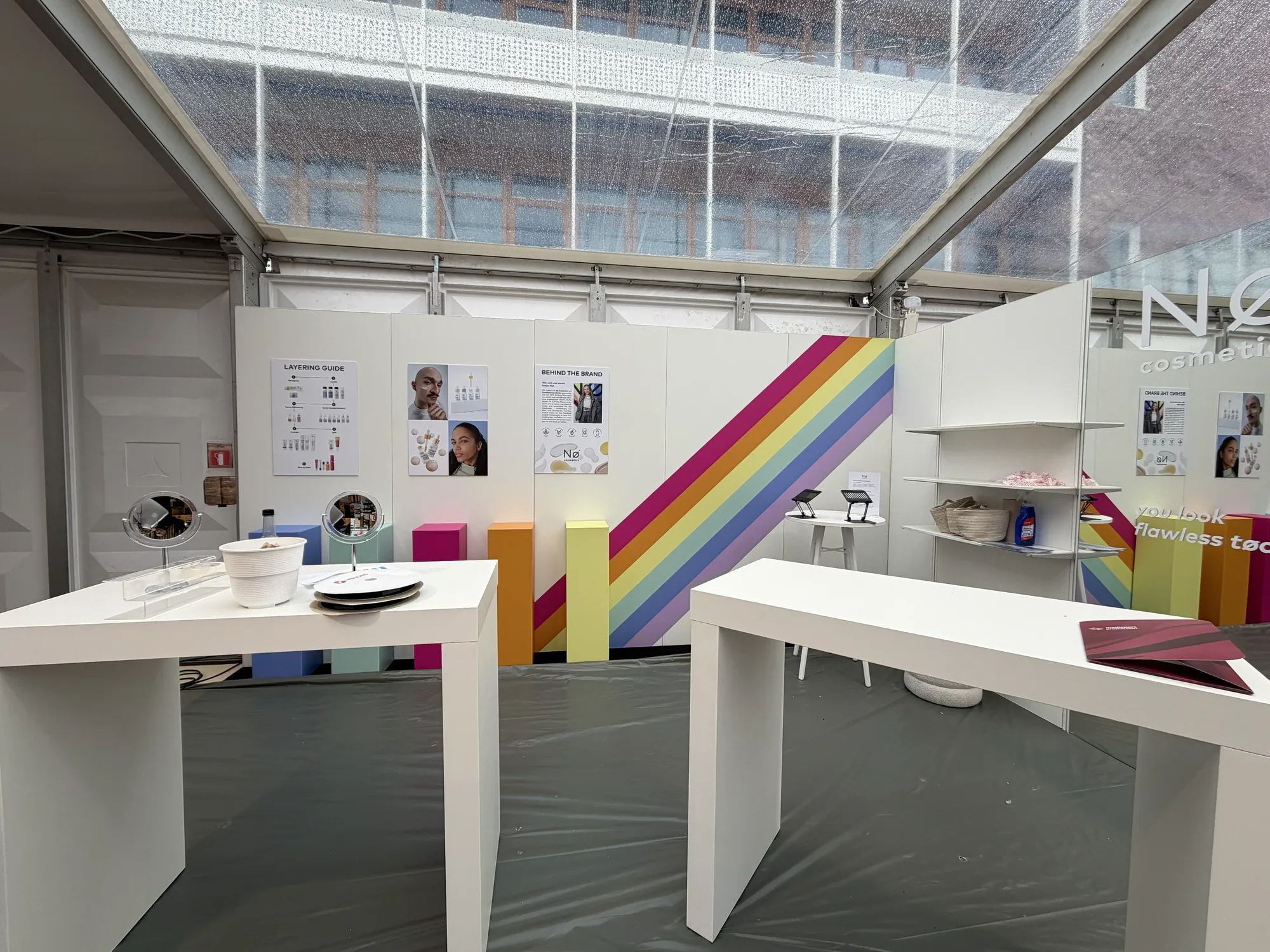 Helle Beauty-Präsentation mit Regenbogenwand und weißen Ausstellungstischen